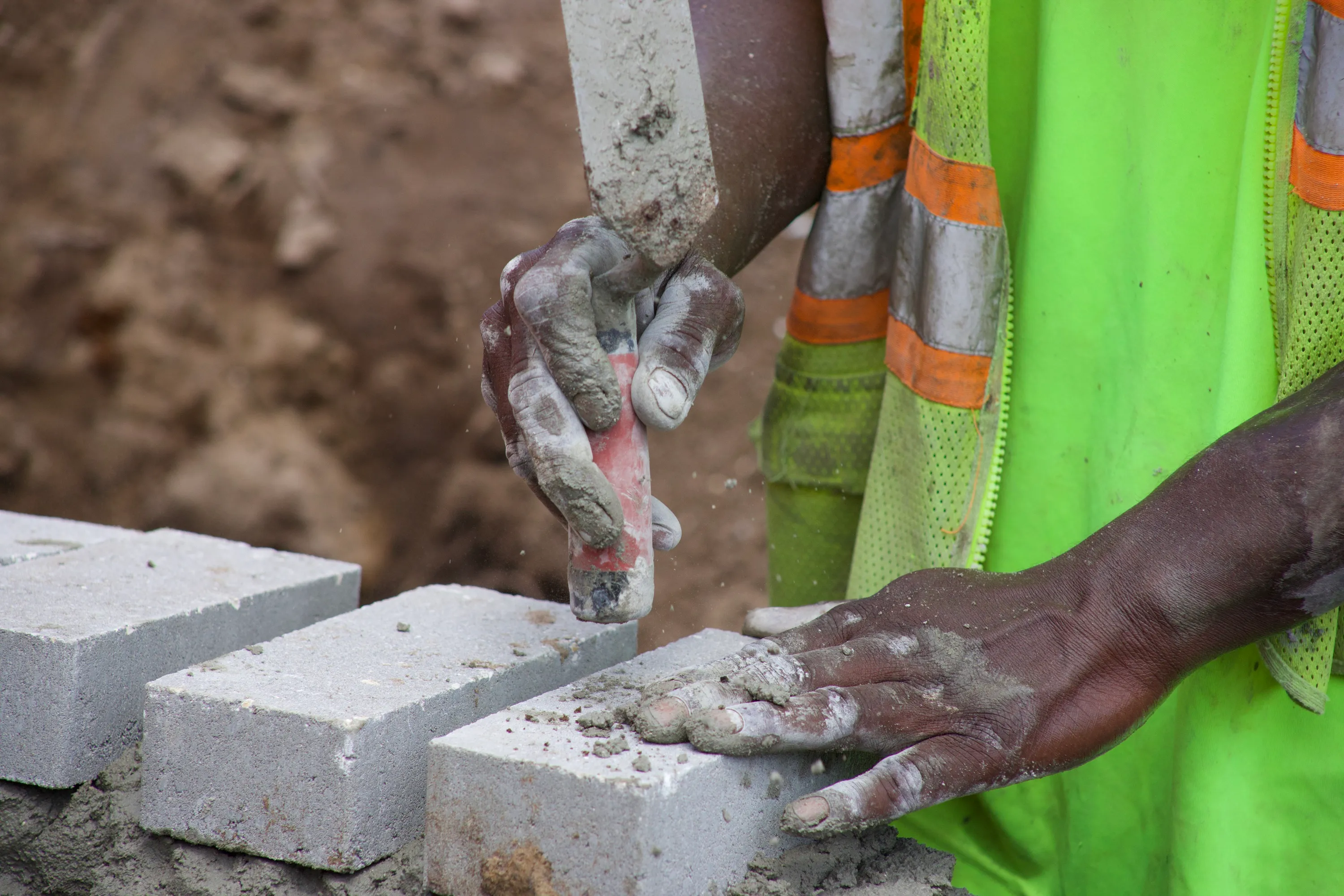 A PDG crew member's hands setting concrete block in fresh mortar