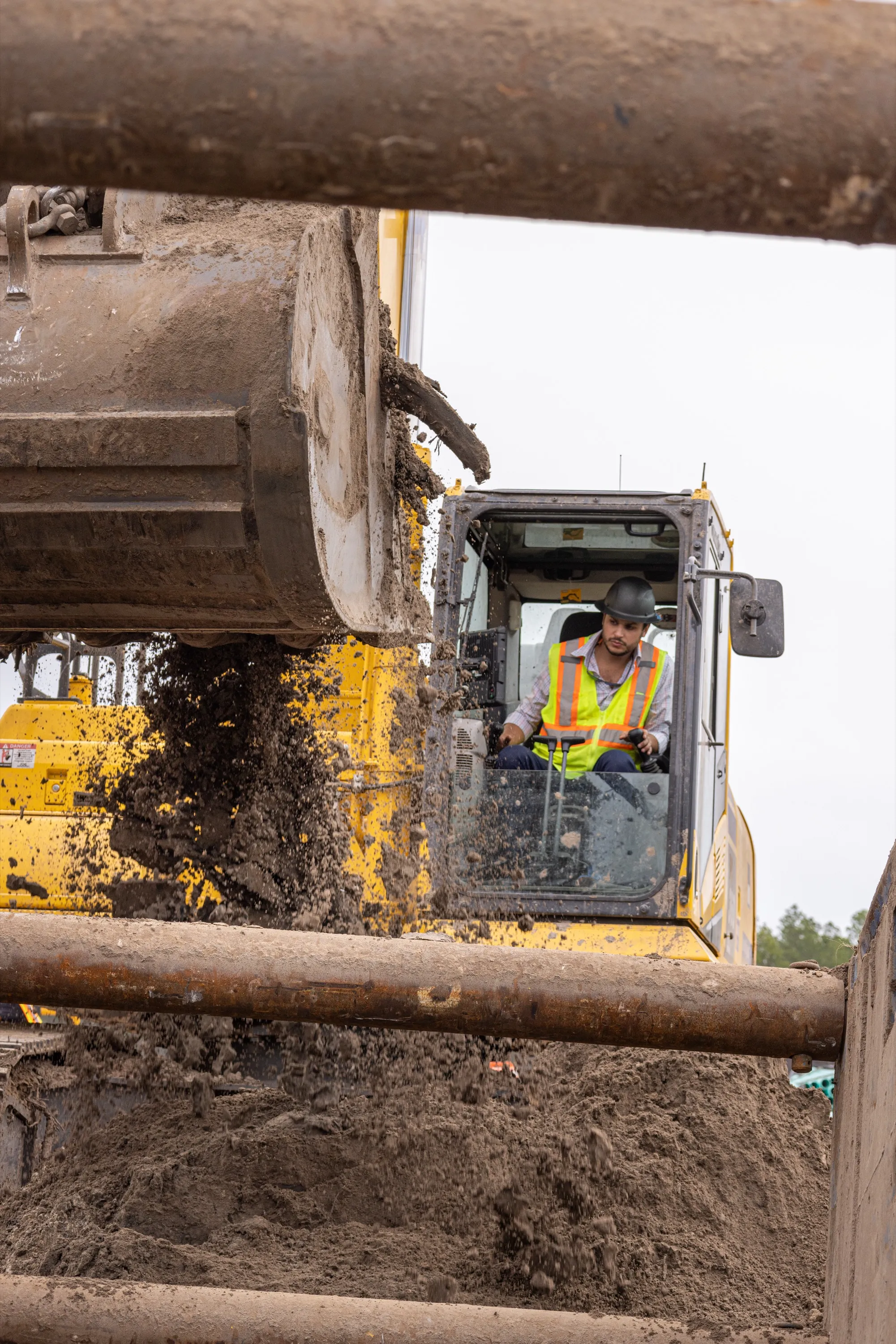 Gabriel at the controls of an excavator, dumping a bucket of spoil